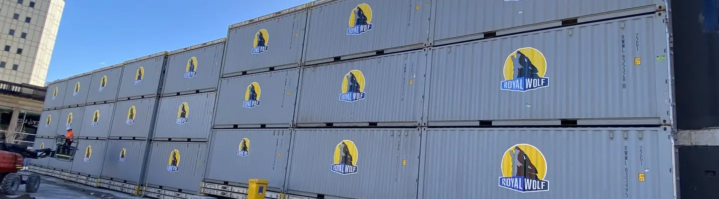 Stacked shipping containers organized and ready for use in a secure storage yard under a clear sky.