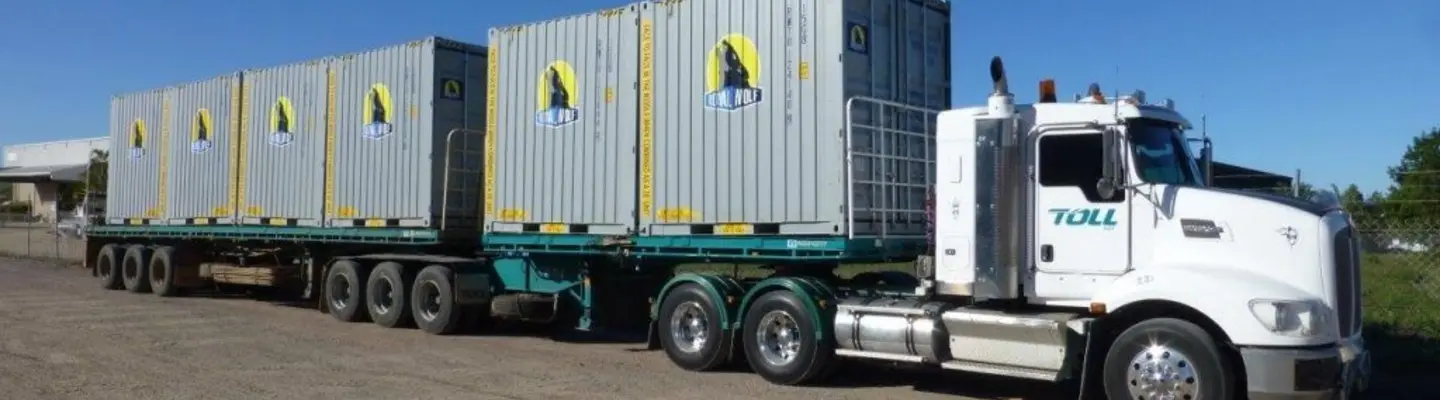 A truck loaded with stacked shipping containers driving on a highway, ready for delivery to a storage or shipping facility.
