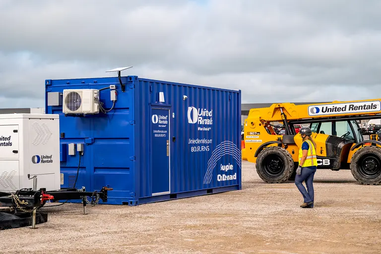 Un empleado de United Rentals caminando hasta un contenedor azul de suministros a pedido en un sitio de trabajo
