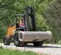Front angled view of an orange CASE forklift carrying a concrete pipe. A worker is operating on an outdoor construction site.