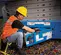Side view of worker in yellow helmet and orange safety vest inspecting a scissor lift in indoor work zone.