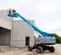 Rear angled view of two workers in safety gear on an extended blue Genie boom lift, elevated on a construction site.