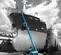 Wide side view of a blue Genie boom lift fully extended in front of large ship's hull with a worker on the platform.