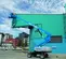 Side view of blue Gania boom lift extended to reach high green container, outdoors in front of buildings.