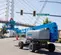 Rear angled view of a blue Genie lift with extended boom, operator using lift at a street intersection.