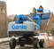 Side view of a blue and gray Genie boom lift with two workers in the elevated platform working on an outdoor construction site.