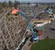 Side wide view of a blue boom lift with an extended arm and worker on platform working on a wooden roller coaster structure.