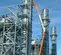 Wide side view of orange and beige boom lift arm and platform with worker, outdoors in front of industrial equipment.