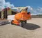 Rear view of orange JLG boom lift with extended arm and basket, on outdoor construction site.