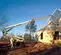 Side view of an orange and beige boom lift lifting roof panels on a home construction, operator in safety gear standing nearby.