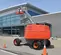 Rear view of an orange and gray Skyjack boom lift with extended arm and worker in basket, outdoors near a building.