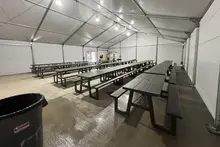 Filas de mesas de picnic oscuras dispuestas dentro de una tienda industrial amplia y bien iluminada, que sirven como sala de descanso temporal.