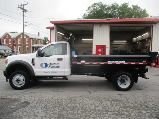 Camión volcador de eje único Ford blanco estacionado afuera de un garaje